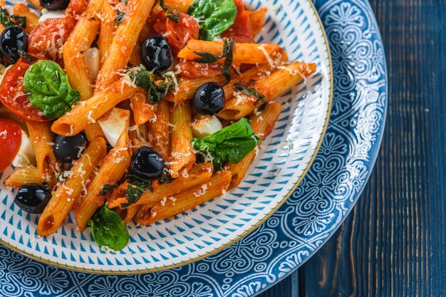 Pasta con pomodorini, mozzarella e spinaci olive, su un tavolo di legno. Stile rustico.