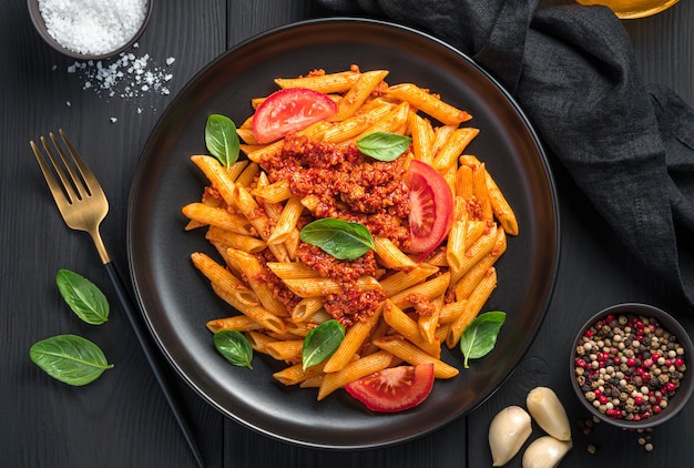 Pasta con ragù di pomodoro e basilico fresco su sfondo nero. Un piatto della tradizione italiana.