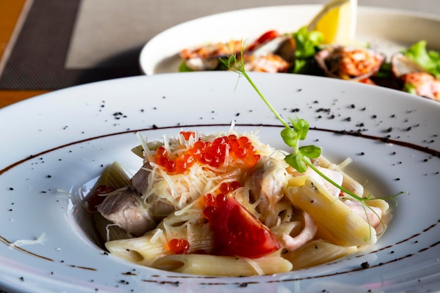 Pasta con salmone, pomodorini e caviale rosso su un piatto bianco in un ristorante. Alta cucina