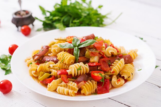 Pasta con salsa di pomodoro con salsiccia, pomodori, basilico verde decorato in piastra bianca su fondo in legno.