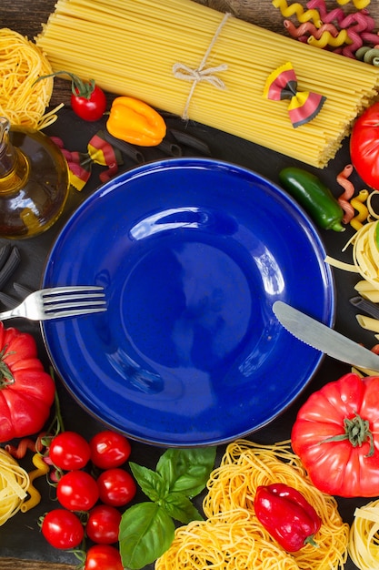 Pasta cruda con ingridients e copia spazio sul piatto blu vuoto