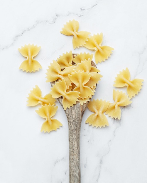 Pasta cruda in cucchiaio di legno su sfondo bianco