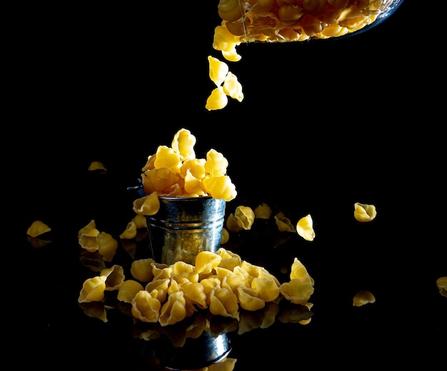 Pasta cruda in vaso di vetro bicchiere di vino in secchio pasta cruda su sfondo nero vista frontale pasta cruda caduta dal posto della mano per testo cannucce di spaghetti lunghe gialle