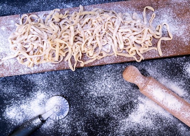 Pasta cruda sulla tavola di legno con il matterello e la taglierina di ruota