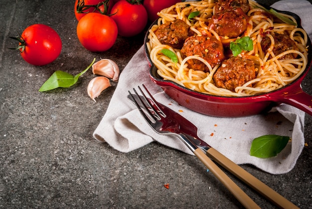 Pasta degli spaghetti con le polpette, salsa al pomodoro del basilico in padella rossa del ghisa, sulla tavola di pietra nera