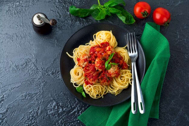 Pasta degli spaghetti con polpette di carne, salsa di pomodoro e basilico su sfondo scuro.