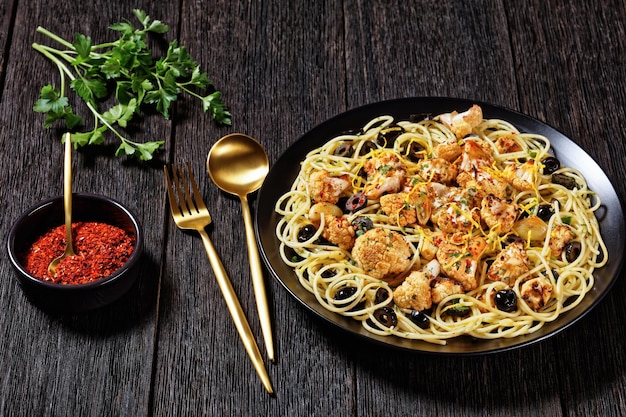 Pasta di cavolfiore arrosto con olive nere e scorza di limone su una piastra nera su un tavolo di legno scuro, piatto, spazio libero