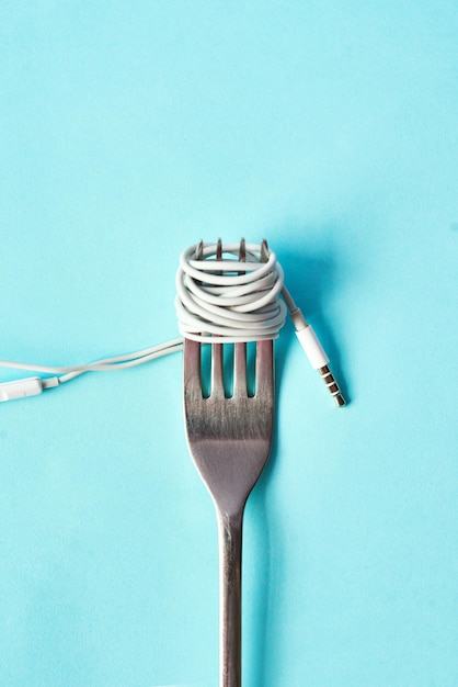 Pasta di cibo o musica e auricolari con forchetta in studio isolati su sfondo blu per consumare contenuti podcast astratto e streaming media con filo su utensili da mangiare per radio audio o suono