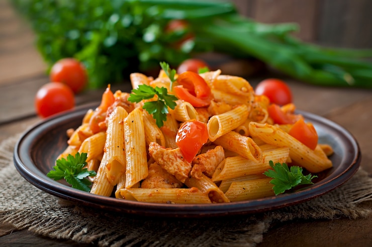 Foto pasta di penne in salsa di pomodoro con pollo e pomodori su un tavolo di legno