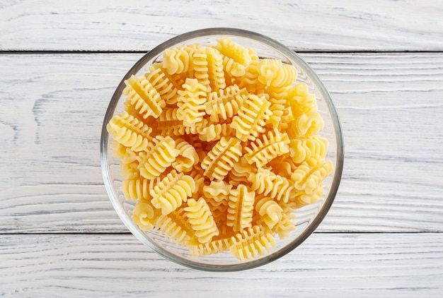 Pasta di radiatori cruda in ciotola di vetro su fondo di legno bianco