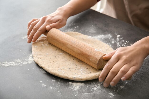 Pasta di rotolamento della donna con i semi di papavero sul primo piano della tavola