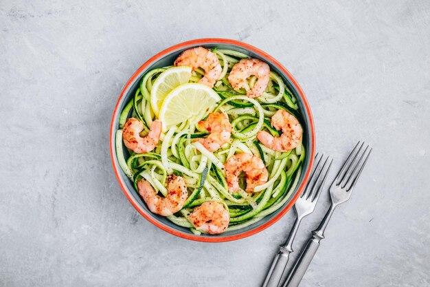 Pasta di spaghetti di zucchine a spirale con gamberetti su sfondo di pietra grigia vista dall'alto