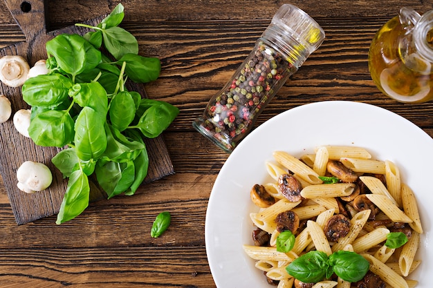 Pasta di verdure vegetariano penne con funghi in ciotola bianca sul tavolo di legno.