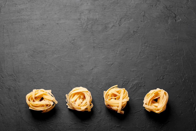 Pasta fresca italiana l su uno sfondo scuro con copia spazio per il testo. Tagliatelle nidi di pasta.