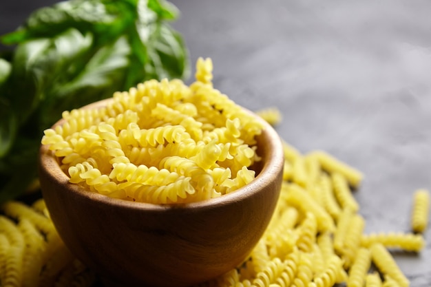 Pasta girandole in ciotola di legno e basilico verde erba su tavola di pietra nera