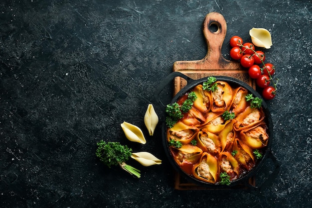 Pasta Grandi gusci di pasta al forno con carne in salsa di pomodoro In padella Su fondo di pietra nera