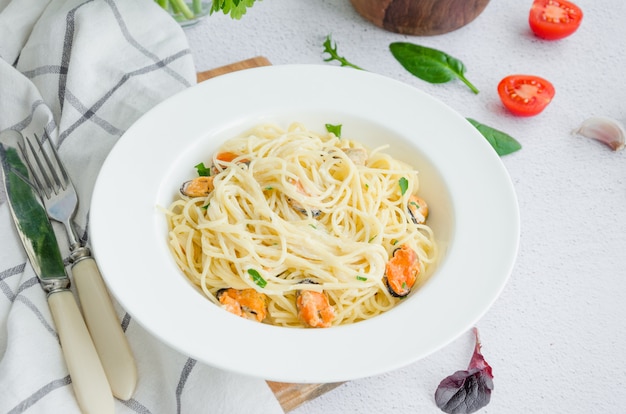 Pasta in salsa cremosa con cozze, formaggio, aglio e prezzemolo su un piatto bianco su un tavolo di pietra chiara.