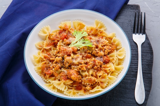 Pasta in salsa di pomodoro bolognese su un supporto nero rotondo su un tovagliolo blu accanto a una forchetta Foto orizzontale