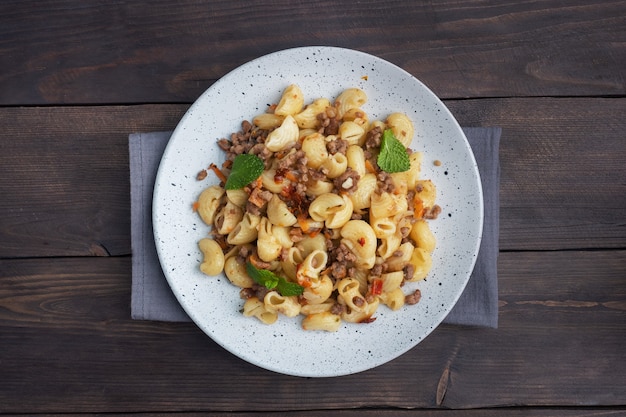 Pasta in umido con carne macinata di manzo e verdure, maccheroni alla marinara alla piastra. Fondo in legno scuro. Copia spazio.