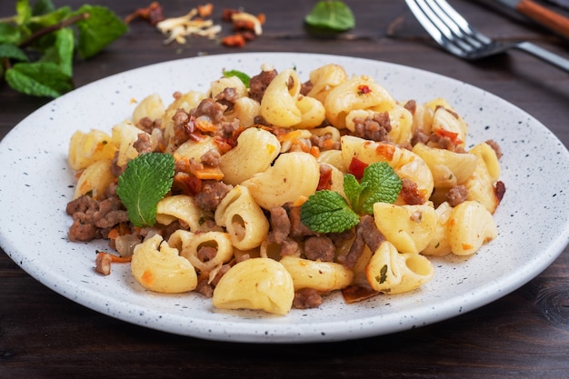 Pasta in umido con carne macinata di manzo e verdure, maccheroni alla marinara alla piastra. Fondo in legno scuro.