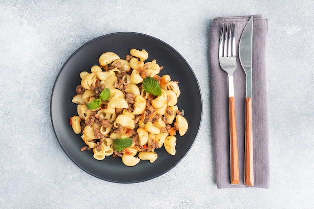 Pasta in umido con carne macinata e verdure, maccheroni alla Marina su un piatto. cemento grigio