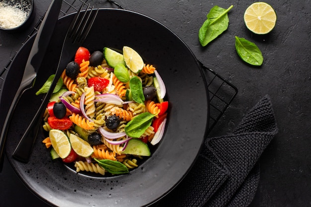 Pasta integrale con verdure su un piatto bianco su sfondo nero di ardesia, pietra o cemento. Vista dall'alto con copia spazio.