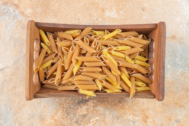 Pasta integrale cruda di penne in una scatola di legno sulla superficie di marmo