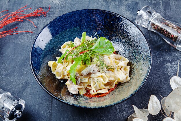 Pasta italiana casalinga fresca e saporita con basilico, il pomodoro ed il fungo in ciotola scura. Cucina italiana. Sfondo di foto di cibo con spazio di copia.