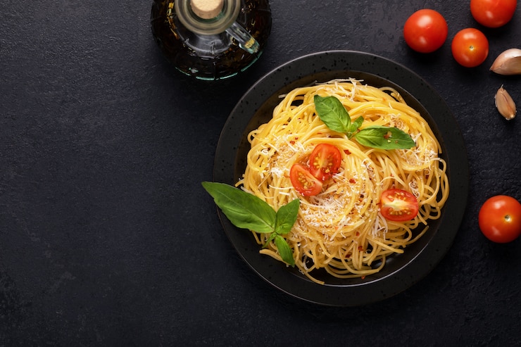 Foto pasta italiana classica appetitosa vegetariana degli spaghetti con basilico, salsa al pomodoro, parmigiano e olio d'oliva sulla banda nera sulla tavola scura. vista dall'alto, orizzontale. copia spazio per il testo.