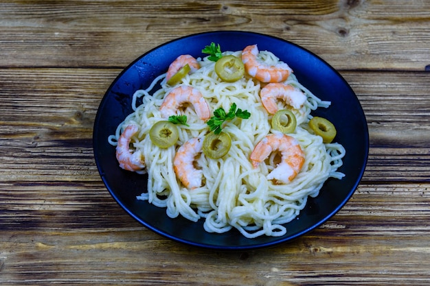 Pasta italiana con gamberi e olive in un piatto nero