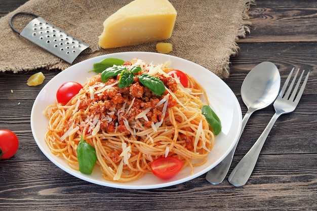 Pasta italiana con salsa bolognese e parmigiano su una tavola di legno rustica.