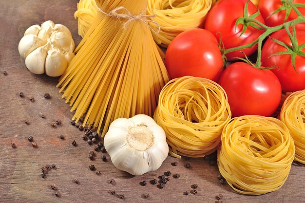 Pasta italiana cruda, ramo di pomodori maturi, aglio e pepe nero su fondo di legno