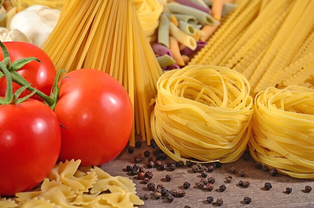 Pasta italiana cruda, ramo di pomodori maturi e pepe nero