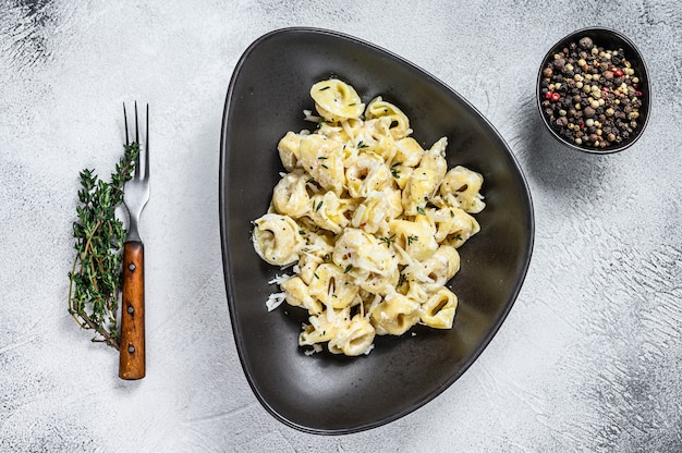 Pasta italiana dei tortellini in salsa di panna con spinaci. Fondo di legno bianco. Vista dall'alto.