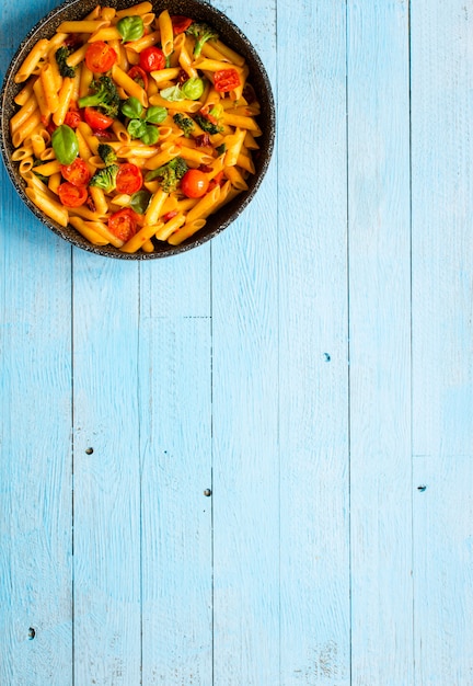 Pasta italiana del penne in salsa al pomodoro e tipo differente di verdure, su un fondo di legno