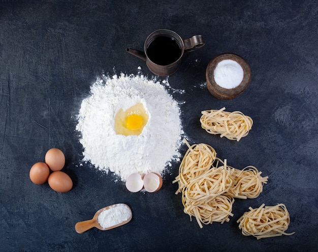 Pasta italiana fatta in casa chiamata fettuccine, uova e farina sul tavolo scuro