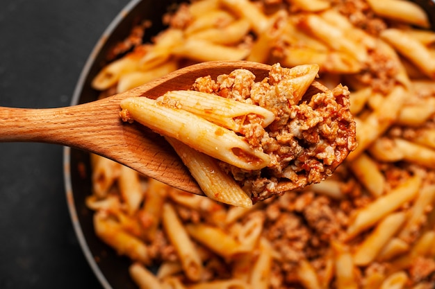 Pasta italiana fresca del penne bolognese sul cucchiaio di legno.