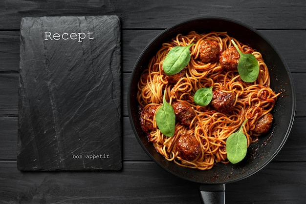 Pasta italiana in salsa di pomodoro con polpette di carne e basilico su uno sfondo di legno scuro con uno spazio vuoto