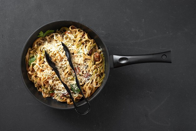 Pasta italiana in una padella con funghi e salsa di panna su sfondo nero vista dall'alto spazio vuoto