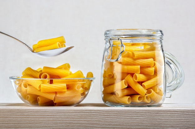 Pasta italiana secca in ciotola di vetro e vaso sulla tavola di legno. Concetto di dieta e cibo.