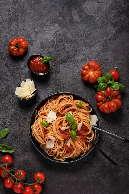 Pasta italiana tradizionale con salsa di pomodoro, basilico e formaggio su sfondo nero, vista dall'alto in basso con spazio di copia