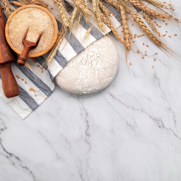 Pasta lievitata fresca fatta in casa appoggiata su un tavolo di marmo con spighe di grano e mattarello.