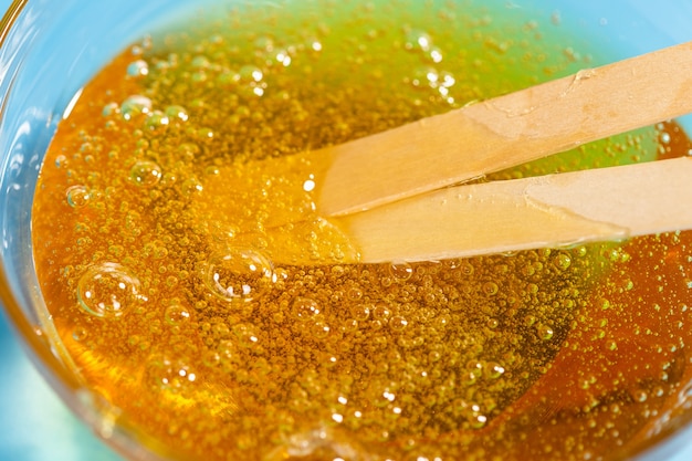 Pasta liquida gialla per zuccherare e bastoncini su blu. Depilazione e concetto di depilazione.