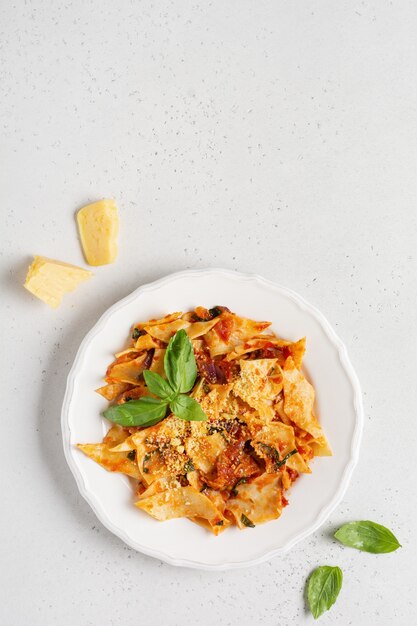 Pasta Maltagliati con salsa di pomodoro classica, parmigiano e basilico su un tavolo leggero di cemento rustico. Piatto italiano tradizionale che serve. Vista dall'alto.