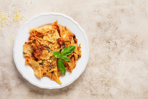 Pasta Maltagliati con salsa di pomodoro classica, parmigiano e basilico su uno sfondo di tavolo luminoso in cemento rustico. Piatto italiano tradizionale che serve. Vista dall'alto.