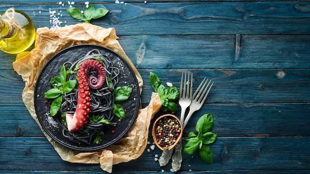 Pasta nera con tentacoli di polpo Frutti di mare su un piatto di pietra Sullo sfondo vecchio Vista dall'alto Spazio libero per la copia