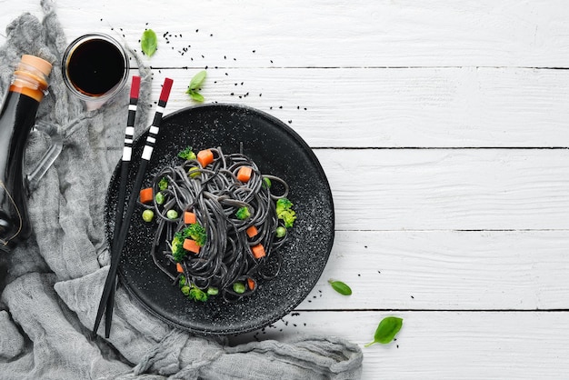 Pasta nera con verdure su un piatto nero Vista dall'alto su uno sfondo di legno bianco Spazio libero per la copia