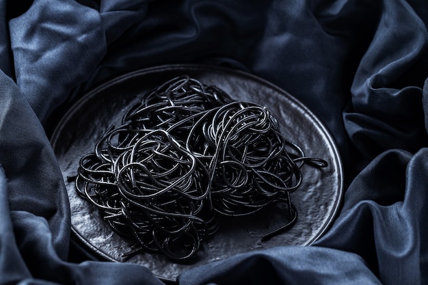 Pasta nera su un piatto nero. Pasta al nero di seppia su fondo scuro. Spaghetti al nero di seppia. Copia spazio. Vista dall'alto