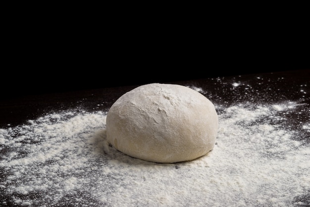 Pasta per pizza o cottura su uno sfondo nero scuro di legno