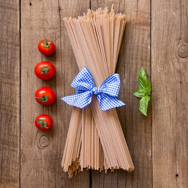 Pasta, pomodori e basilico degli spaghetti sulla vista superiore del fondo di legno